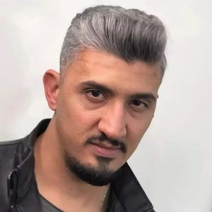 Homem de cabelo grisalho penteado para o lado, com barba curta.