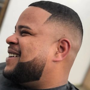 Homem sorrindo de perfil, com degradê alto e barba cheia desenhada.